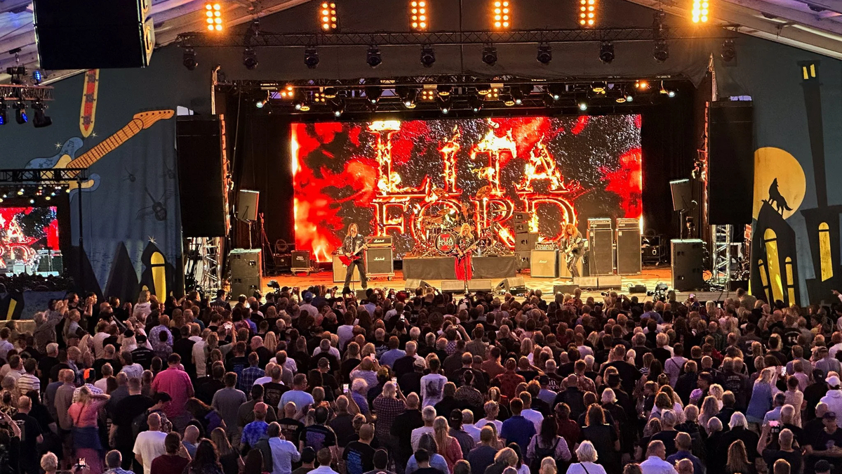 crowd enjoying a live concert on stage with colorful lights and a vibrant backdrop visible